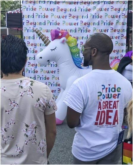 A Power Beyond Pride photo backdrop with a rainbow unicorn and a team member in a Pride Power shirt